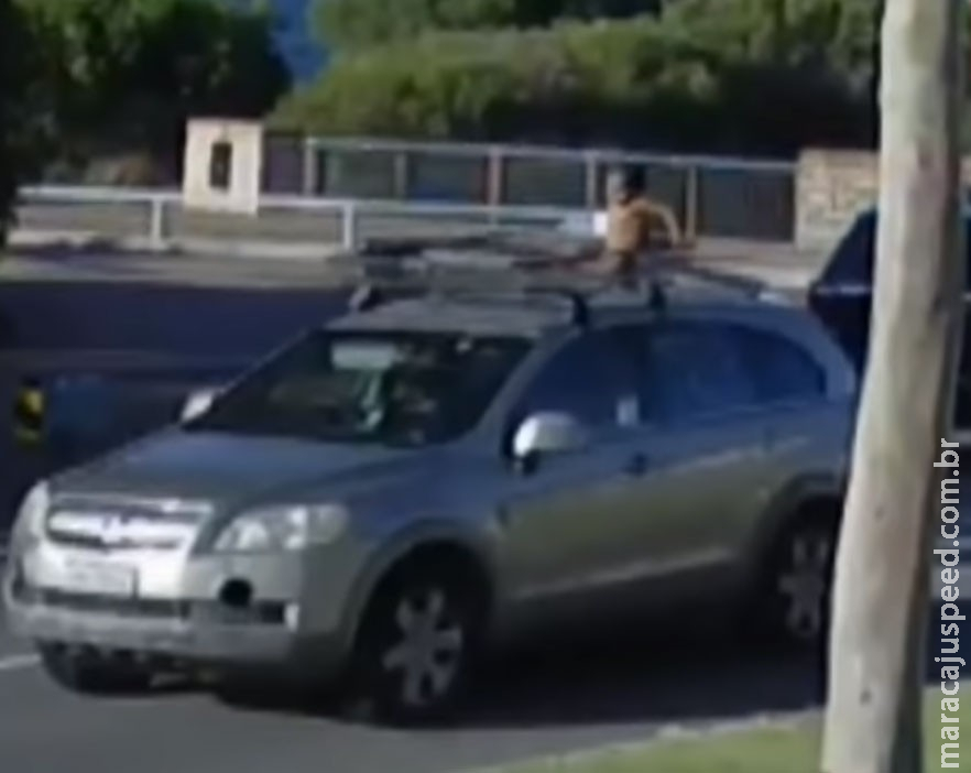 Criança de 4 anos vestida só de fraldas é vista sobre teto de carro, enquanto mãe dirige