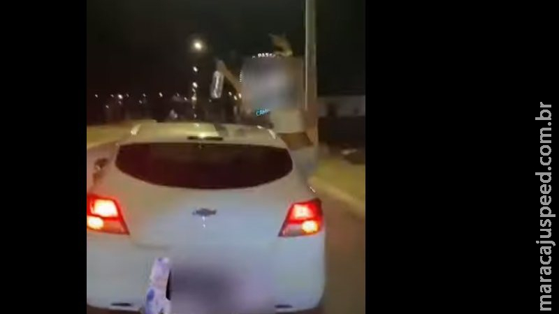 Com garrafa na mão, mulher é filmada sentada em janela de carro em movimento Com garrafa na mão, mulher é filmada sentada em janela de carro em movimento