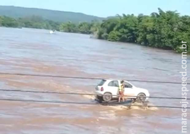 Carro é transportado por dois barcos no rio Taquari em Coxim